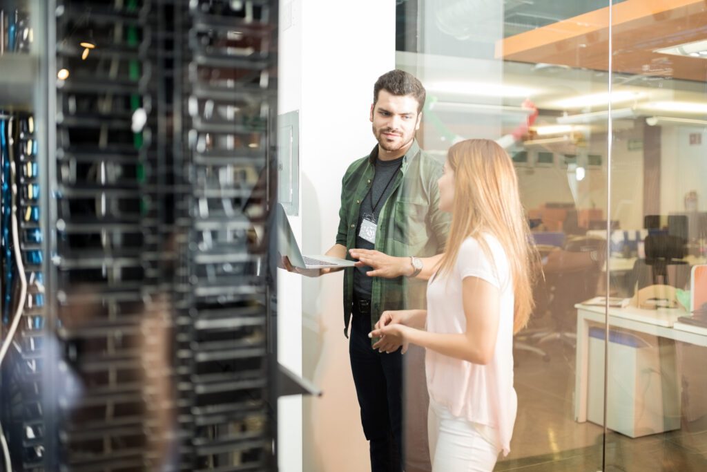 two business people standing server room with laptop discussing